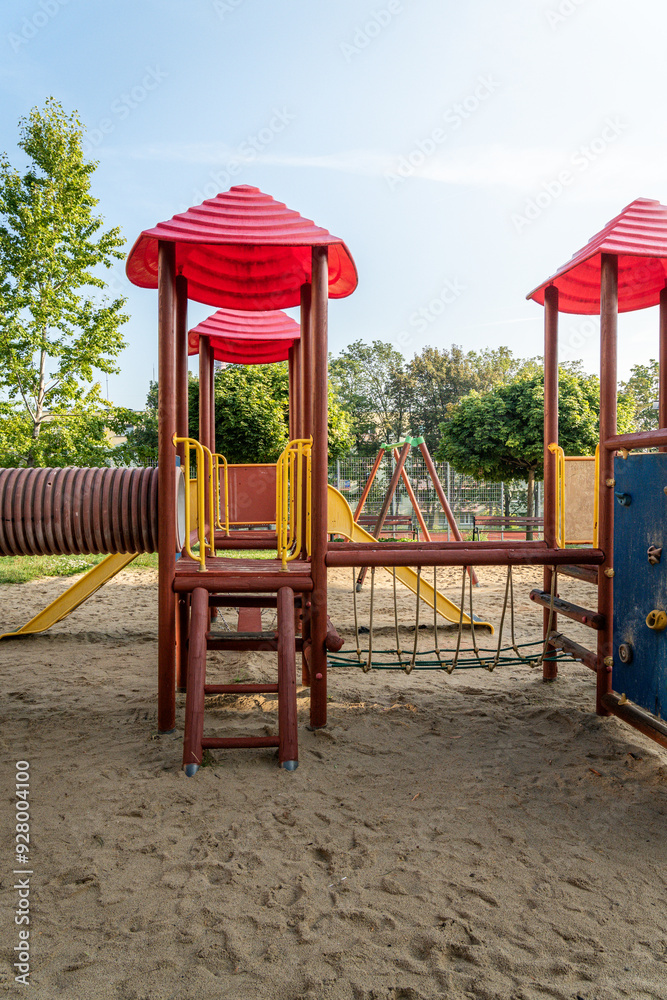 Play structure with red roofs and climbing features in a sunny playground located in a park Play structure with red roofs and climbing features in a sunny playground located in a park