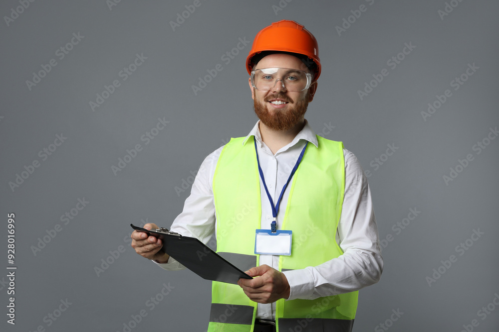 Engineer in hard hat and goggles holding clipboard on grey background Engineer in hard hat and goggles holding clipboard on grey background