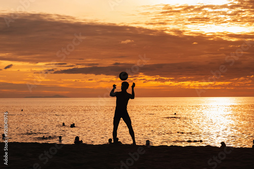 Silhouette of an Asian male player with a ball playing traditional sepak takraw football on the beach by the sea at sunset photo