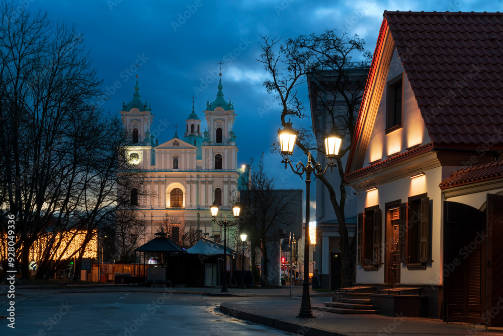 View of the recreated historical buildings on Zamkovaya Street and the Cathedral of St. Francis Xavier in the background at dusk with night lighting, Grodno, Belarus View of the recreated historical buildings on Zamkovaya Street and the Cathedral of St. Francis Xavier in the background at dusk with night lighting, Grodno, Belarus