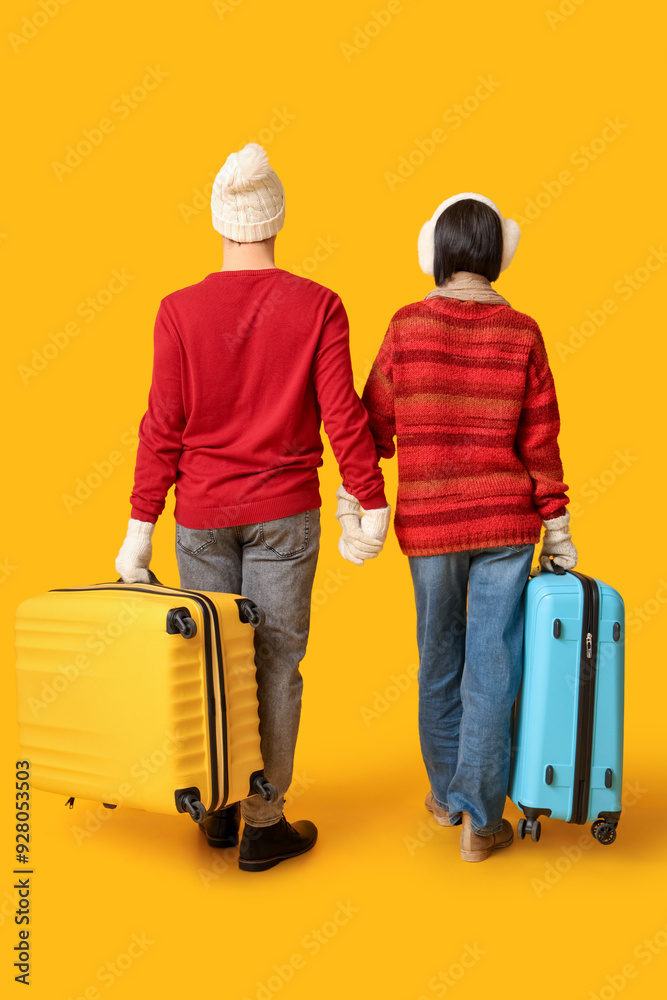 Beautiful young couple with suitcases on yellow background, back view. Winter vacation concept Beautiful young couple with suitcases on yellow background, back view. Winter vacation concept