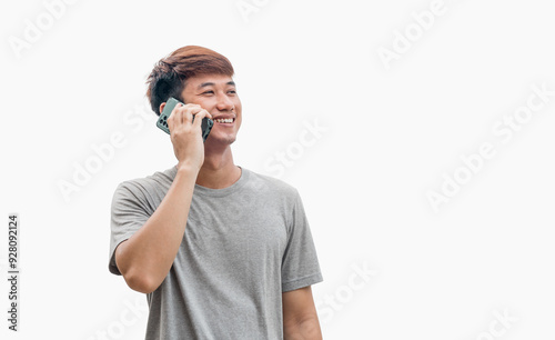 Young Asian man in his 20s wear a gray t-shirt is talking on the phone standing on a gray background. Long-distance communication concept