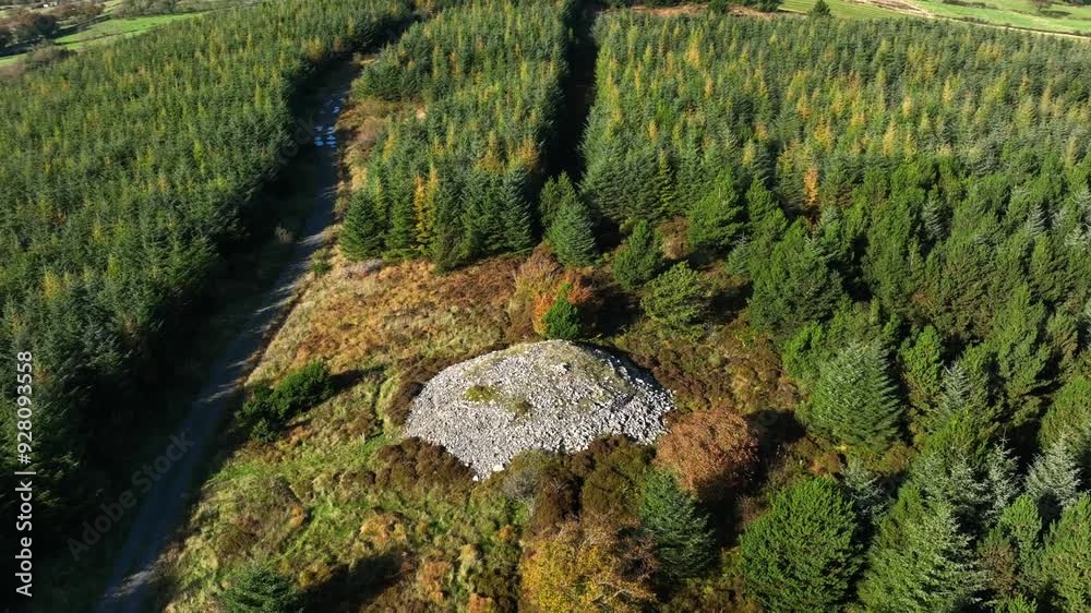 Mullyash Kerbed Cairn, County Monaghan, Ireland, November 2022. Drone orbits counter clockwise rising to a Bird's Eye view above the Neolithic Monument with forest casting shadows on the dirt road. Mullyash Kerbed Cairn, County Monaghan, Ireland, November 2022. Drone orbits counter clockwise rising to a Bird's Eye view above the Neolithic Monument with forest casting shadows on the dirt road.