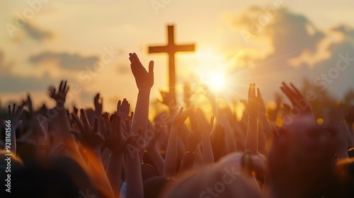 A crowd with raised hands in worship under a sunset sky with a cross in the background