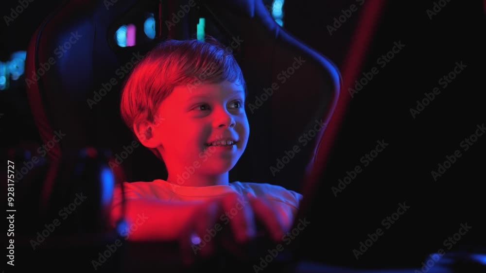 Portrait of a cheerful little boy playing video games in a computer club at night with neon lights. The boy is happy and raises his hands up. The child's addiction to gambling. Portrait of a cheerful little boy playing video games in a computer club at night with neon lights. The boy is happy and raises his hands up. The child's addiction to gambling.