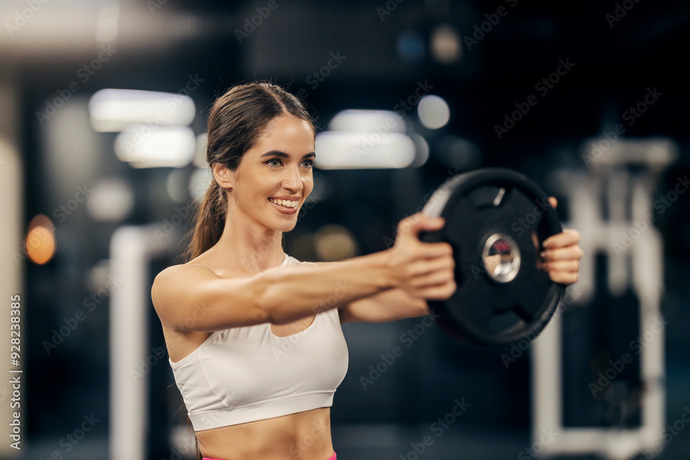 Portrait of happy sporty woman in trendy sportswear practicing with weight plate.