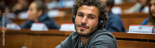 Young Male Student with Headphones in Lecture Hall Attentively Listening During Class