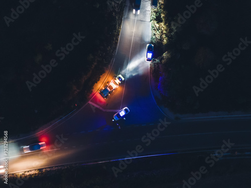 Aerial view of night car accident with involved pedestrian. Roadside assistance loads wrecked car, police direct traffic