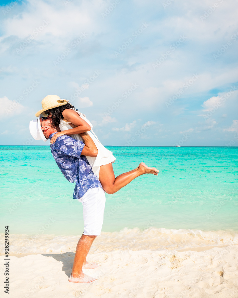 Happy, young couple in white summer clothes enjoying their vacation having kissing each other on a tropical beach.Maldives honeymoon holiday destination background. Fulidhoo island Happy, young couple in white summer clothes enjoying their vacation having kissing each other on a tropical beach.Maldives honeymoon holiday destination background. Fulidhoo island