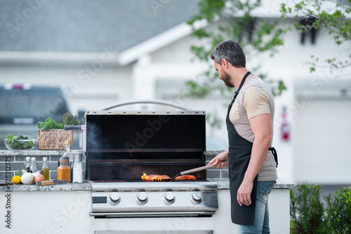 Cropped image of handsome man is making grill barbecue outdoors on the backyard. Bbq party. Bbq meat, grill for picnic. Roasted on barbecue. Man preparing barbeque in the house yard.