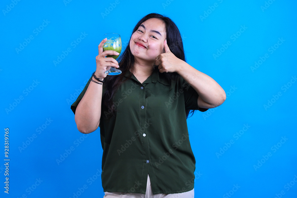 Plus Size Woman Giving Thumb Up Holding And Showing Green Smoothie Healthy Juice Isolated on Blue Background Plus Size Woman Giving Thumb Up Holding And Showing Green Smoothie Healthy Juice Isolated on Blue Background