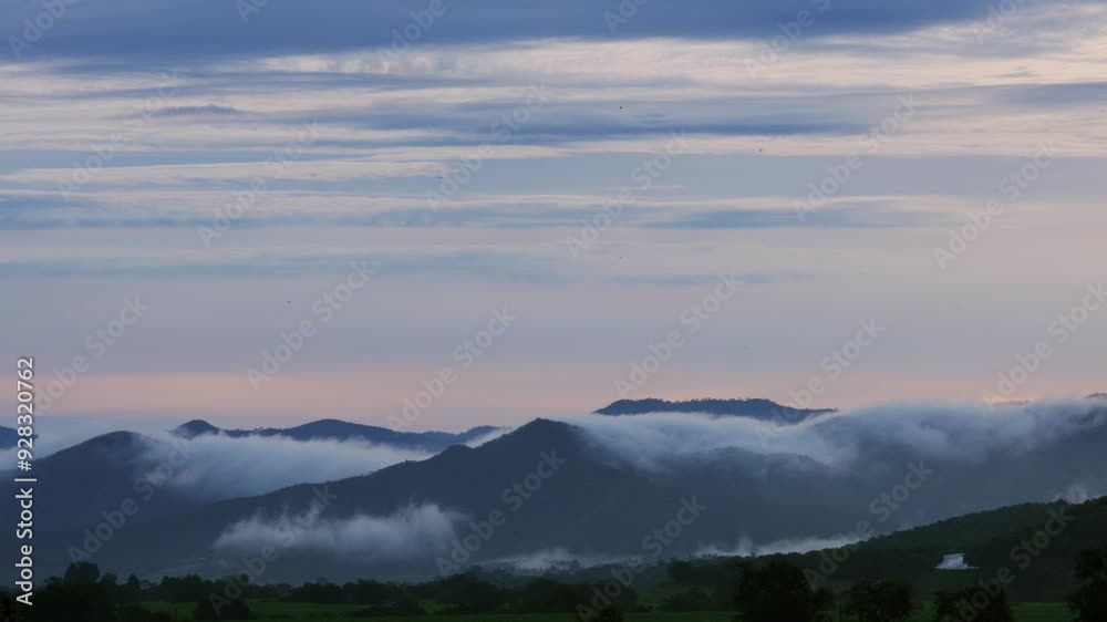 Timelapse of fast-moving clouds on light blue morning sky above foggy haze-covered mountains Timelapse of fast-moving clouds on light blue morning sky above foggy haze-covered mountains