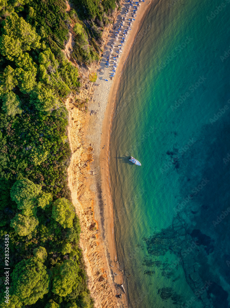 Aerial overhead sunset view of Mantraki beach with emerald sea and lush pine tree forrest at the island of Skiathos, Sporades, Greece