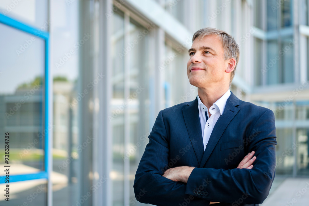 Smiling businessman standing in front of office building with crossed arms Smiling businessman standing in front of office building with crossed arms
