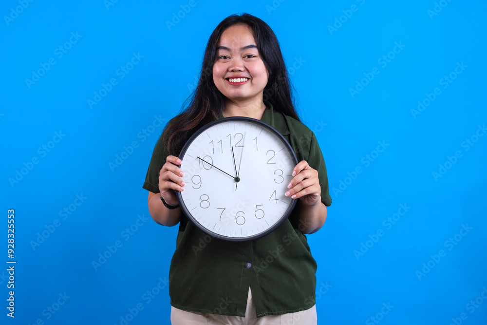 Chubby Young Asian Girl Holding And Showing Clock Isolated On Blue Background. Chubby Young Asian Girl Holding And Showing Clock Isolated On Blue Background.
