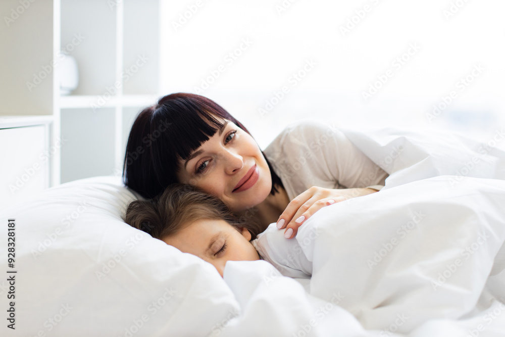 Mother and child cuddling in bed with white blankets, creating warm and loving moment. Mother smiling while child peacefully sleeps, capturing essence of family, comfort, care.