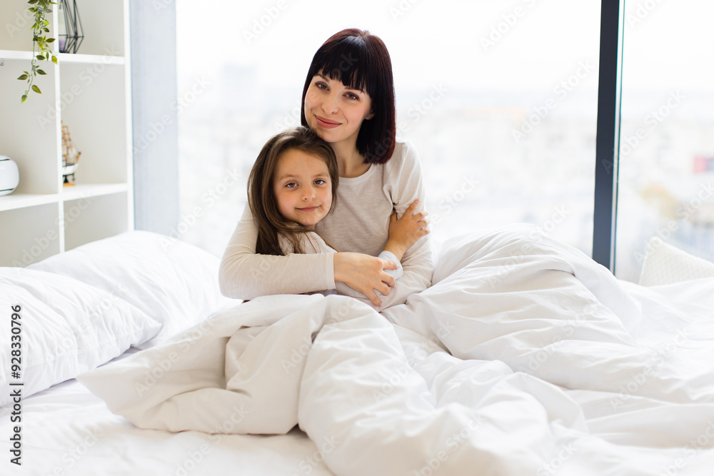 Mother and daughter hugging in bed in bright, cozy bedroom. They look content and happy, sharing a moment of love and comfort. Bonding between parent and child in a serene, peaceful setting. Mother and daughter hugging in bed in bright, cozy bedroom. They look content and happy, sharing a moment of love and comfort. Bonding between parent and child in a serene, peaceful setting.