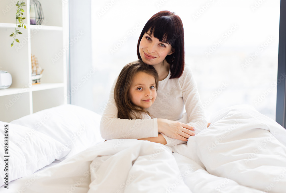 Mother and daughter hugging in bed. Mother and child enjoying cozy morning, sharing love and togetherness. Bright and serene bedroom setting.