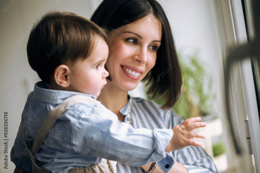 Smiling woman and baby looking through window at home Smiling woman and baby looking through window at home