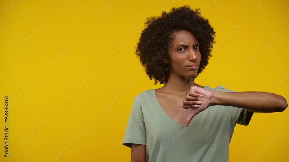 Serious Young Woman Giving Thumbs Down Gesture Against a Yellow Background Serious Young Woman Giving Thumbs Down Gesture Against a Yellow Background