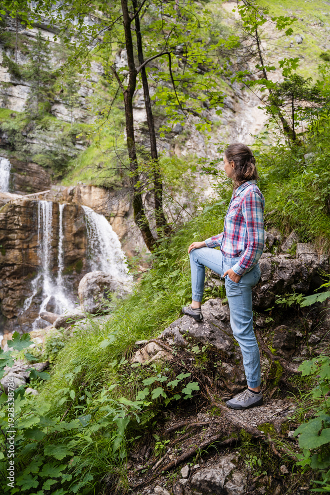 Woman standing and looking at waterfall in forest Woman standing and looking at waterfall in forest