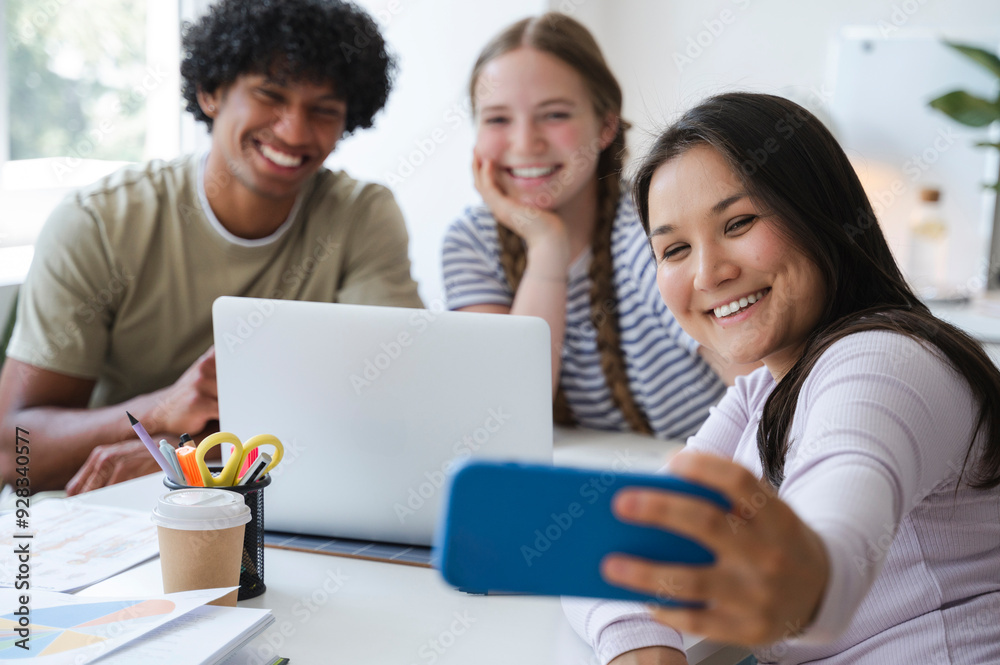Smiling woman taking selfie through smart phone with friends at home Smiling woman taking selfie through smart phone with friends at home