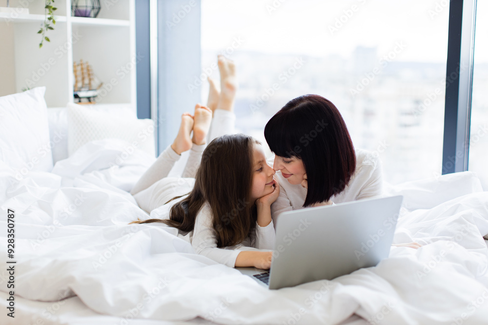 Mother and daughter enjoying quality time together on bed with laptop. Family bonding, love, and connection are highlighted in bright natural light from window. Mother and daughter enjoying quality time together on bed with laptop. Family bonding, love, and connection are highlighted in bright natural light from window.