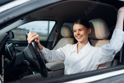 Φωτογραφία Woman driving new car in a parking lot, smiling with hand on steering wheel