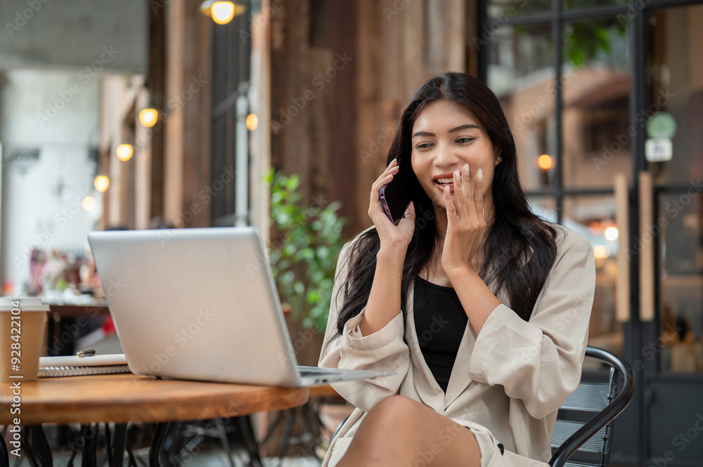 Gorgeous, carefree Asian businesswoman is enjoying talking on the phone at a cafe, working remotely. Gorgeous, carefree Asian businesswoman is enjoying talking on the phone at a cafe, working remotely.