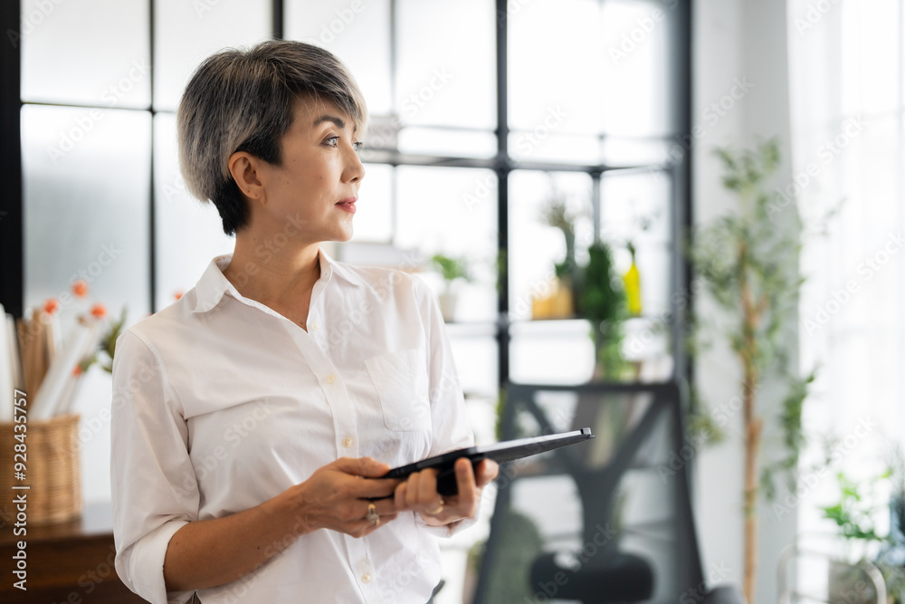 A female architect stands thoughtfully, holding a tablet in a modern office filled with design books and materials, ready to present her ideas A female architect stands thoughtfully, holding a tablet in a modern office filled with design books and materials, ready to present her ideas