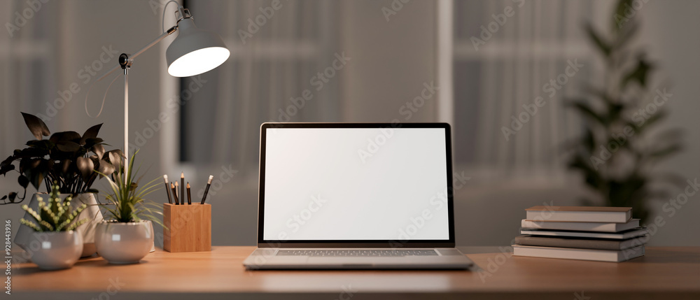 Fototapeta premium A laptop computer with a white-screen mockup and decor on a wooden table in a room at night.