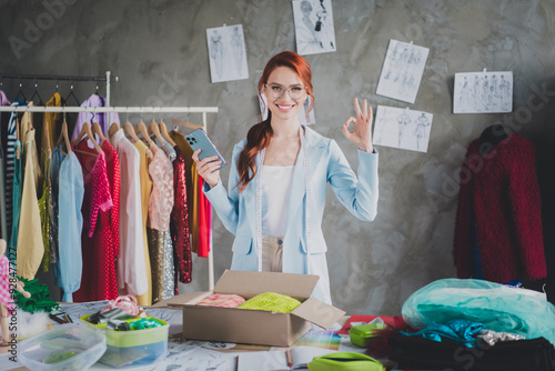 Portrait of nice designer dressmaker lady smart phone okey symbol loft interior office indoors photo