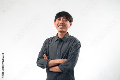 A smiling Asian man in a dark grey button-up shirt stands confidently with arms crossed against a plain white background, ideal for professional headshots, corporate profiles, or personal branding