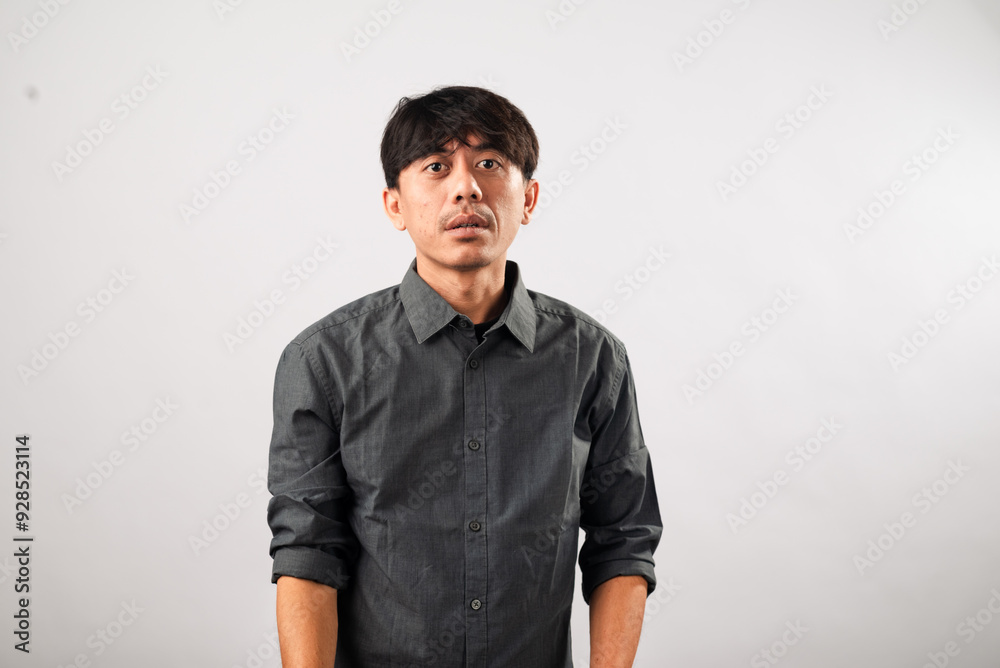 Fototapeta premium A smiling Asian man in a dark grey button-up shirt leans slightly forward with a friendly expression, standing against a plain white background, ideal for personal branding, casual