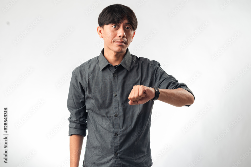 An Asian man in a gray shirt checking the time on his wristwatch, with a focused expression. The background is plain white, emphasizing his attention to the time An Asian man in a gray shirt checking the time on his wristwatch, with a focused expression. The background is plain white, emphasizing his attention to the time