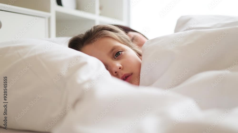 Mother and daughter lying in bed resting peacefully. Child smiling with contentment while cuddling with mother under white bed sheets. Scene highlights family bond, warmth, love, and comfort. Mother and daughter lying in bed resting peacefully. Child smiling with contentment while cuddling with mother under white bed sheets. Scene highlights family bond, warmth, love, and comfort.