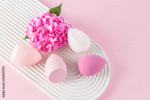 Beautiful beauty blender sponges for applying liquid cosmetics on a white embossed podium with flower. top view. Makeup tool. pink background. closeup