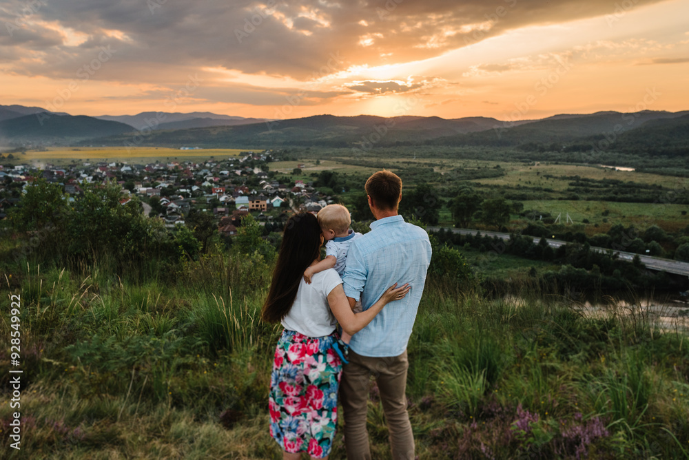 Mom, dad embrace baby looking at sunset. Happy family holiday on summer day. Mother, father, baby in mountains. Parents hugging child. Spend time together. Back view. Mom, dad embrace baby looking at sunset. Happy family holiday on summer day. Mother, father, baby in mountains. Parents hugging child. Spend time together. Back view.
