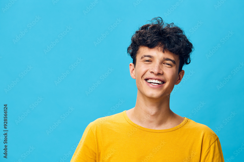 Smiling young man with curly hair in a bright yellow t shirt against a vibrant blue background, conveying happiness and energy, ideal for lifestyle and youth oriented concepts Smiling young man with curly hair in a bright yellow t shirt against a vibrant blue background, conveying happiness and energy, ideal for lifestyle and youth oriented concepts