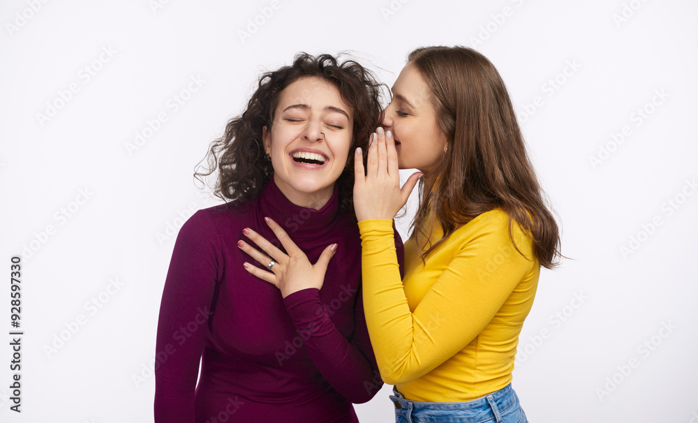 Two women share a secret, one whispering into the other's ear, both laughing and enjoying the moment. Two women share a secret, one whispering into the other's ear, both laughing and enjoying the moment.