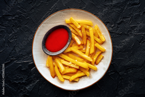 French fries with tomato sauce, overhead flat lay shot, a plate of potato chips on a black stone background