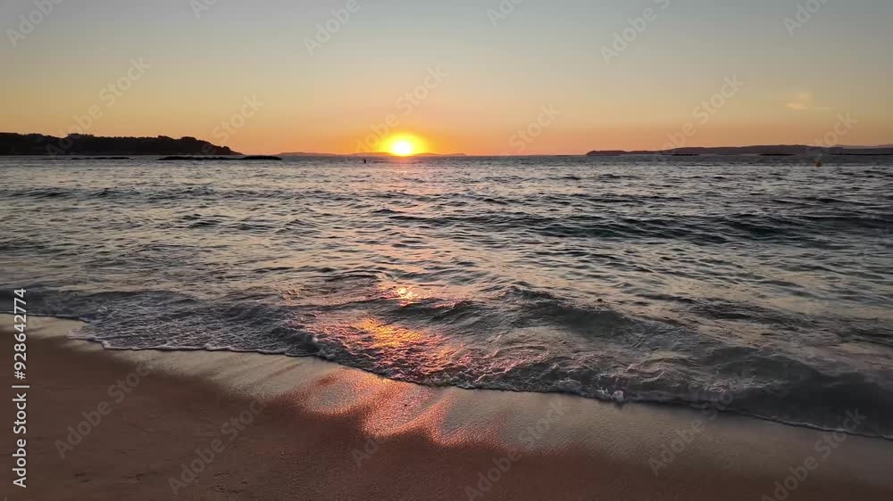 A tranquil beach scene in Bueu - Pontevedra featuring the setting sun over a calm ocean with gentle waves lapping onto the sandy shore, evoking a sense of peace and relaxation.