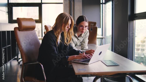 Collaboration in a Modern Workspace Two Women Work Together on a Laptop, Sharing Ideas and Solutions, Highlighting Teamwork and Professional Growth in a Contemporary Setting