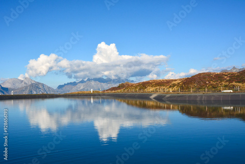 A view of a large lake in front of the mountains in which the blue sky with clouds is reflected. Natural tourist landscape