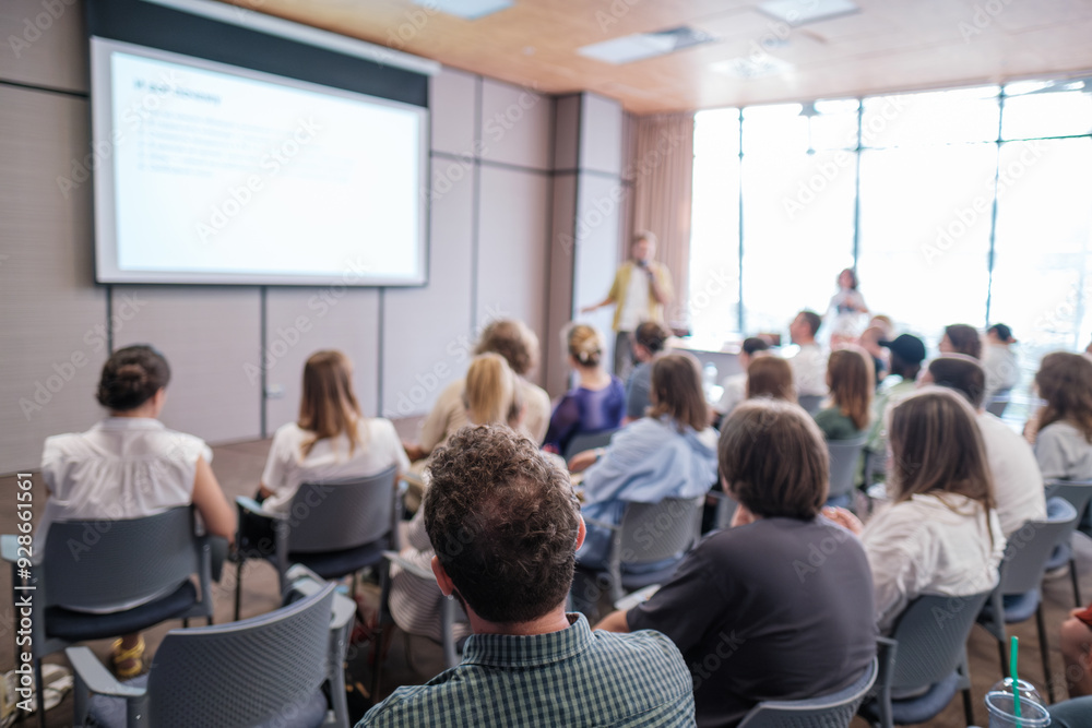 Fototapeta premium Attendees sit attentively as speaker presents during business conference. Bright, modern meeting room enhances learning experience while promoting collaboration and focus among participants.