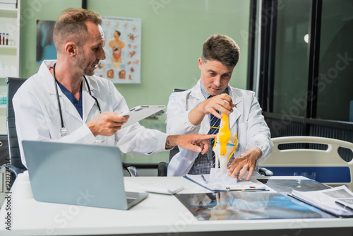 Caucasian middle-aged male doctor and Italian scientific researcher are seated at desk, discussing innovative antiviral drug inventions, with a monitor displaying the latest technology advancements.