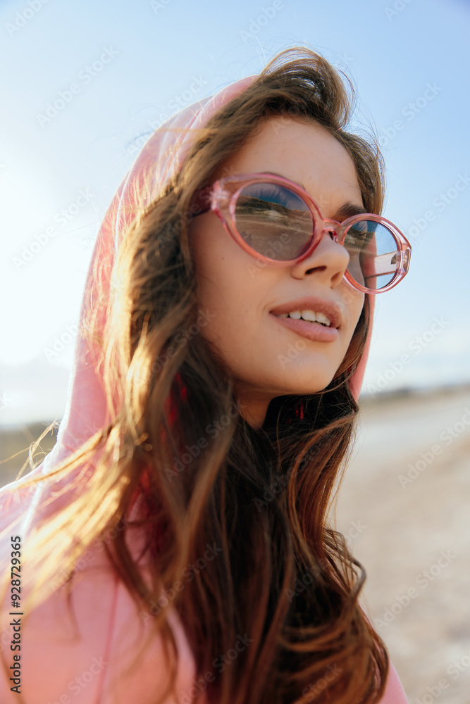 Trendy woman in pink hoodie and sunglasses enjoying the sunny desert beach