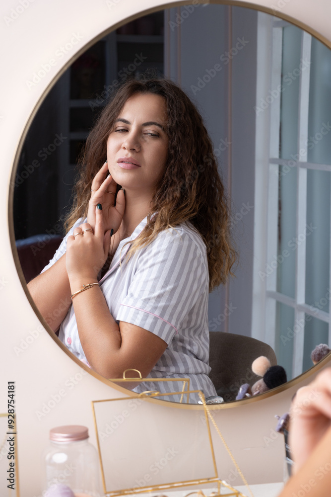 A beautiful curly-haired girl in striped pajamas preens herself in front of the mirror. A woman makes up in the morning, chooses jewelry. A woman looks in the mirror in her bedroom, smile