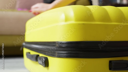 A young woman packs a yellow suitcase for a vacation trip. close-up