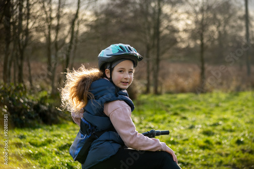 Smiling Girl with Helmet Enjoying a Winter Bike Ride in a Sunlit Park